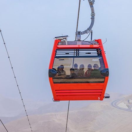 Tolip Resort El Galala Majestic Айн Сохна Екстериор снимка The photo shows a red gondola lift suspended in the air, traveling along cables. Inside the gondola, a group of people can be seen. The background features a hazy landscape, possibly mountains or hills, indicating an elevated area. The scene conveys 