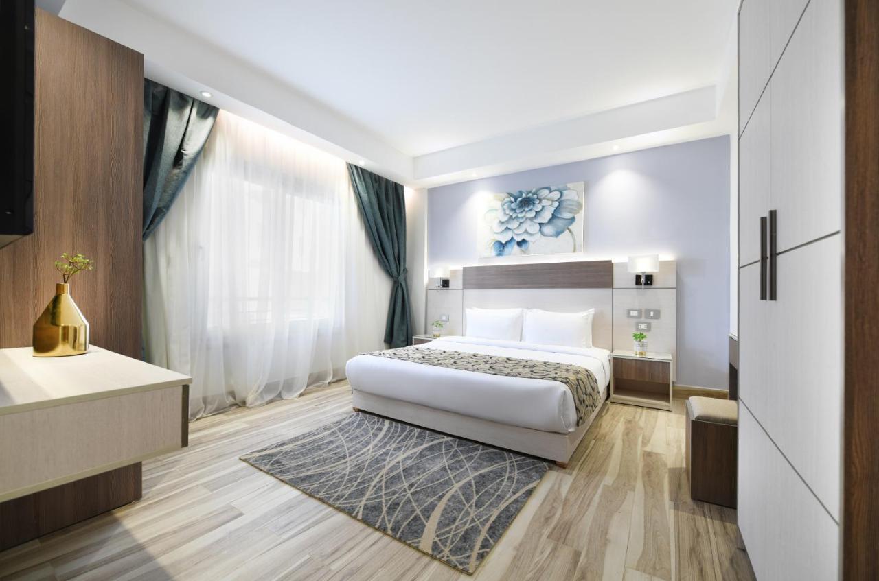 Tolip Resort El Galala Majestic Айн Сохна Екстериор снимка The photo shows a modern bedroom with a clean and stylish design. It features a large bed with white bedding positioned against a wall. Above the bed, there is a decorative artwork, possibly a floral design. The room has large windows with sheer curt