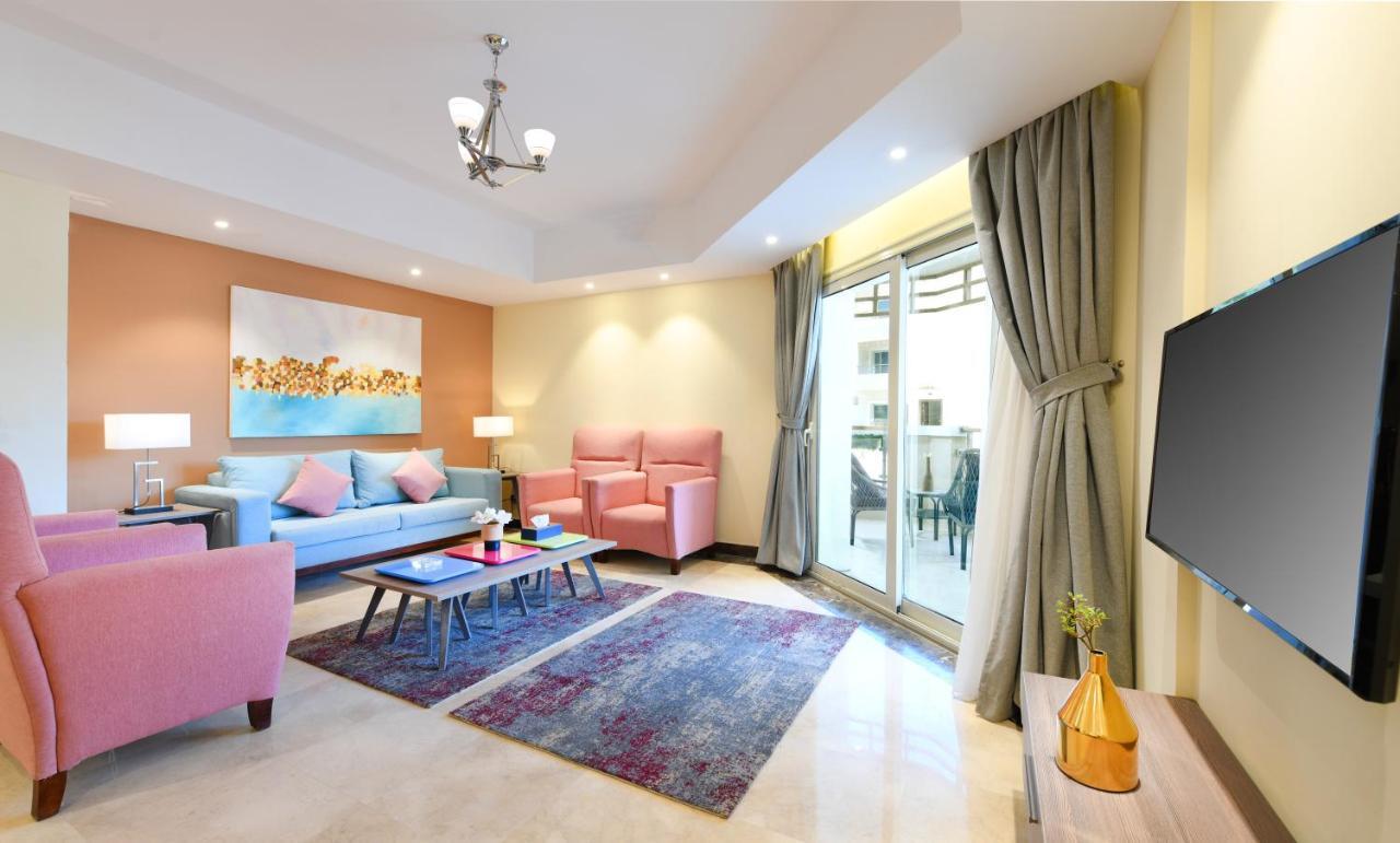 Tolip Resort El Galala Majestic Айн Сохна Стая снимка The photo shows a modern living room that features a cozy and stylish design. There is a light blue sofa adorned with pastel pink cushions, accompanied by two pink armchairs. A coffee table sits in front, placed on a colorful area rug that adds warmt