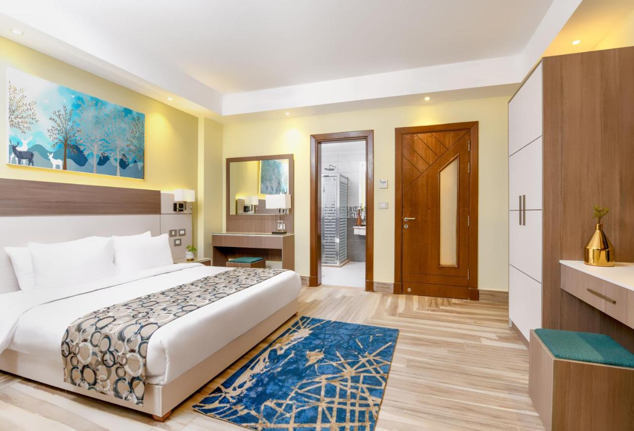 Tolip Resort El Galala Majestic Айн Сохна Екстериор снимка The photo shows a well-decorated hotel room. There is a large bed with white linens and a decorative throw blanket. The room features a wooden wardrobe and a bedside table with lamps. A colorful rug is placed on the floor, adding warmth to the space.