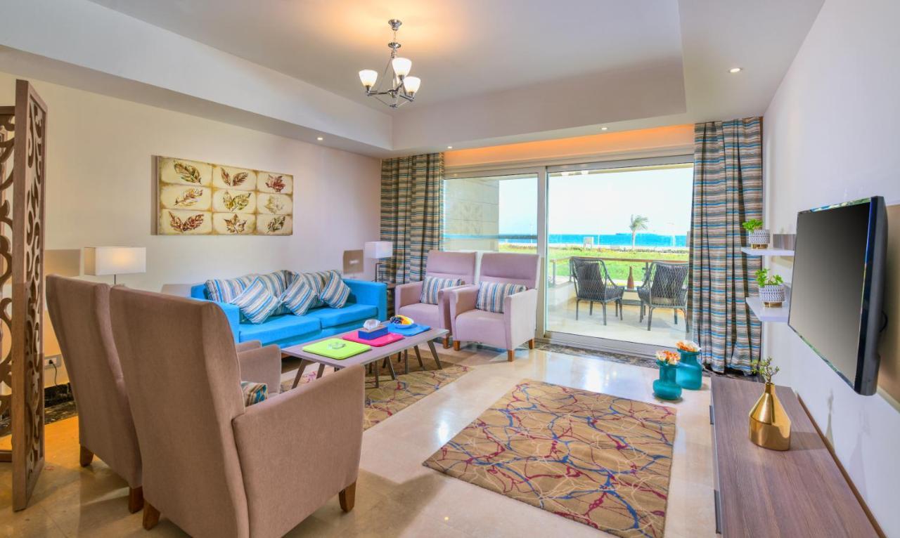 Tolip Resort El Galala Majestic Айн Сохна Екстериор снимка The photo shows a bright and modern living room. It features a blue sofa with decorative cushions, two light-colored armchairs, and a coffee table. A large area rug adds warmth to the space, which is decorated with a subtle pattern. The walls have so