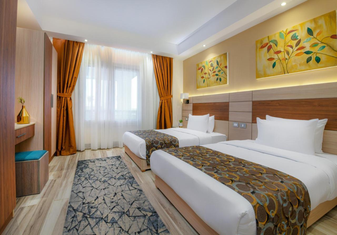 Tolip Resort El Galala Majestic Айн Сохна Екстериор снимка The photo shows a modern hotel room with two single beds, each covered with white linens and decorative brown bed throws. The walls are painted in warm colors, and there are two pieces of artwork featuring floral and leaf designs above the beds. The 