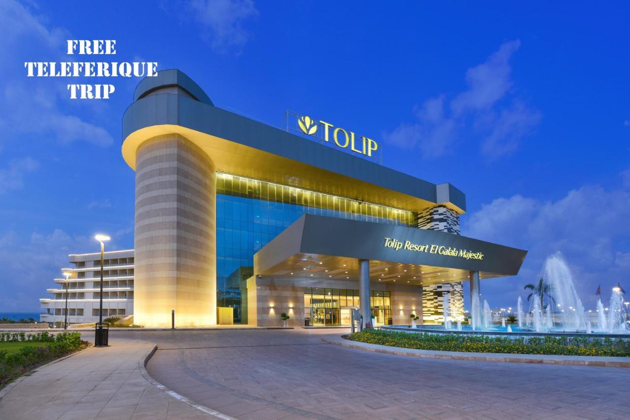 Tolip Resort El Galala Majestic Айн Сохна Екстериор снимка The photo shows a modern hotel building named "Tolip Resort & Spa," featuring a sleek architectural design with large glass windows. The hotel is illuminated against a twilight sky, showcasing its prominent signage. In the foreground, there is a well