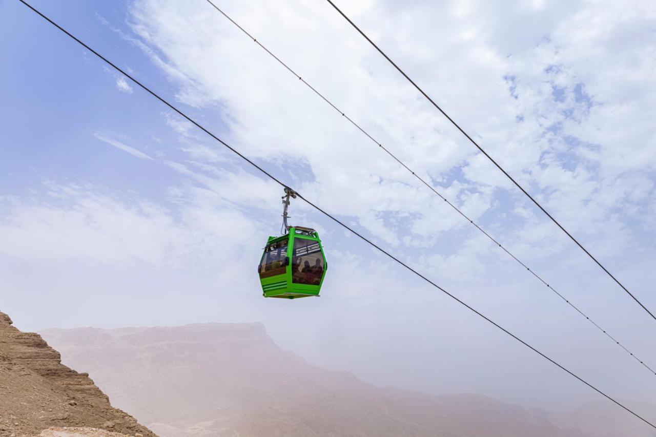 Tolip Resort El Galala Majestic Айн Сохна Екстериор снимка The photo shows a green cable car suspended in the air, traveling along overhead cables. The backdrop features a hazy landscape, likely mountainous or elevated terrain, with a cloudy sky. The scene suggests a scenic transportation method, possibly us