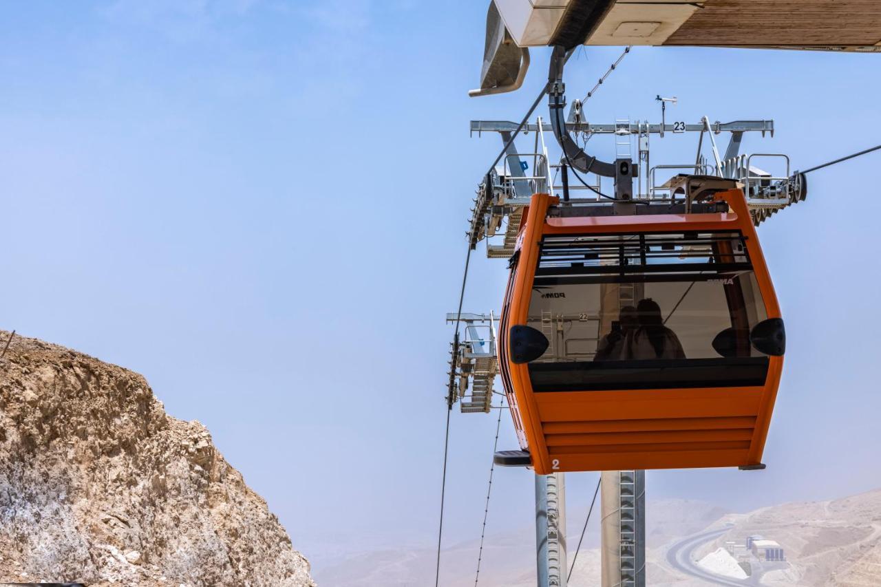 Tolip Resort El Galala Majestic Айн Сохна Екстериор снимка The photo shows an orange gondola or cable car hanging on a cable system. The gondola appears to be suspended in the air above a rocky landscape, with a clear sky in the background. There are supporting cables and structures visible, indicating that 