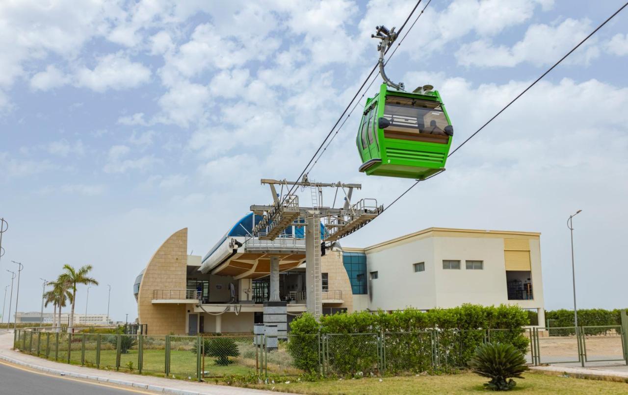 Tolip Resort El Galala Majestic Айн Сохна Екстериор снимка The photo shows a cable car or gondola system in operation, featuring a green-colored gondola. It is suspended from cables and moving towards a station, which appears to be a modern building with a unique architectural design. The station has large w