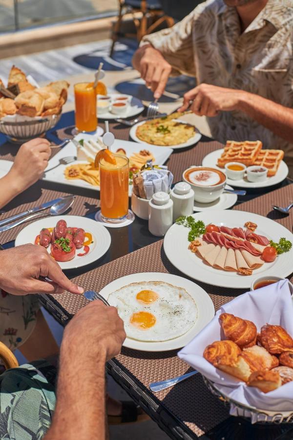 Tolip Resort El Galala Majestic Айн Сохна Екстериор снимка The photo features a spread of breakfast dishes on a table. There are two sunny-side-up eggs on one plate, surrounded by various food items, including slices of ham, sausages, and fresh tomatoes. Another plate holds a serving of waffles. A bowl with 