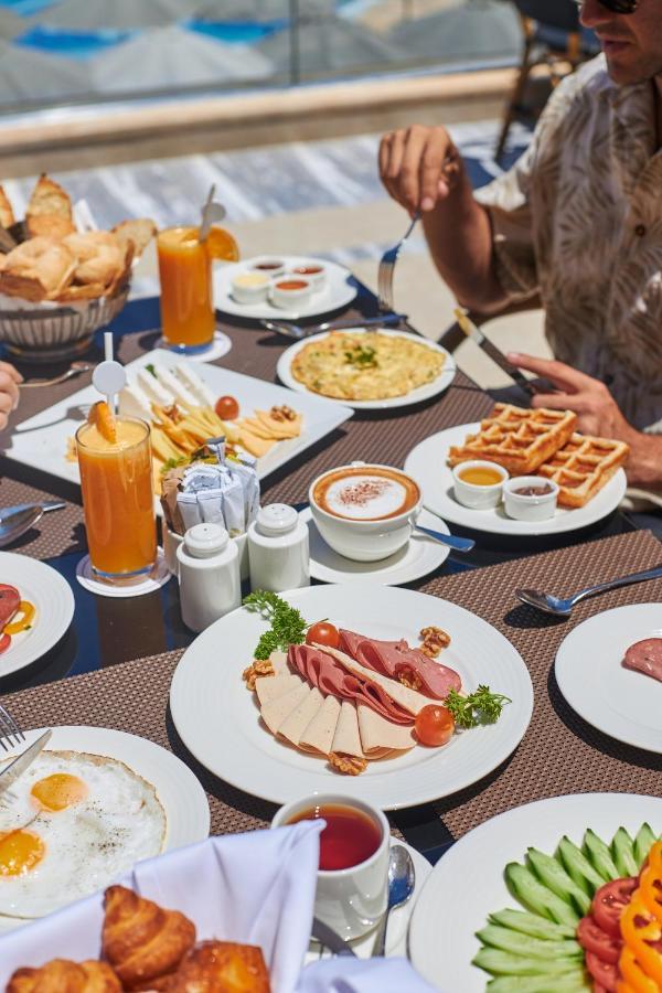 Tolip Resort El Galala Majestic Айн Сохна Екстериор снимка The photo shows a breakfast spread laid out on a table. There are several plates with a variety of food items, including:

1. **Sliced Cold Cuts**: A plate featuring various cold meats, accompanied by garnishes like cherry tomatoes and lettuce.
2. **