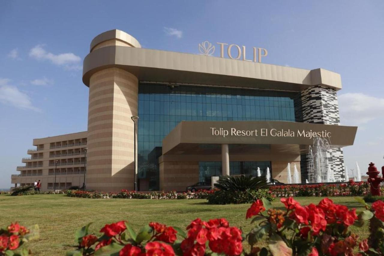 Tolip Resort El Galala Majestic Айн Сохна Екстериор снимка The photo shows a modern hotel building named "Tolip Resort El Galala Majestic." The structure features a distinctive architectural design with large glass windows and a prominent entrance. Surrounding the building are well-maintained lawns and vibra