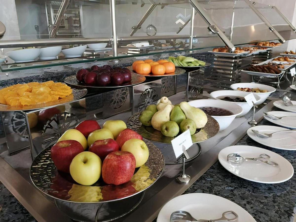 Tolip Resort El Galala Majestic Айн Сохна Екстериор снимка The photo displays a buffet setup featuring an assortment of fresh fruits arranged on several tiered trays. There are red and green apples, pears, grapes, and oranges. Adjacent to the fruit display, there are several bowls containing various other fo