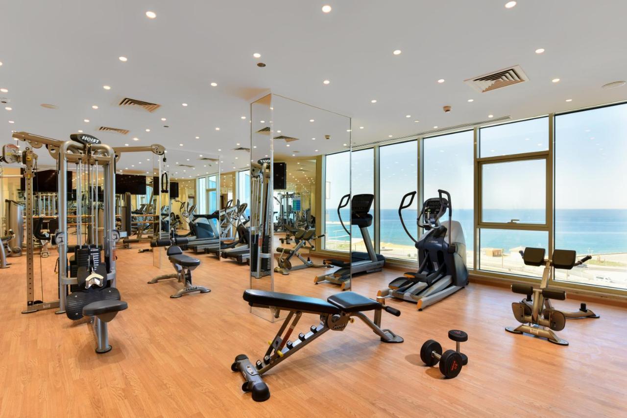 Tolip Resort El Galala Majestic Айн Сохна Екстериор снимка The photo shows a modern gym interior with a variety of fitness equipment. There are cardio machines like treadmills and ellipticals, along with strength training equipment such as free weights and benches. The gym features large windows that offer a