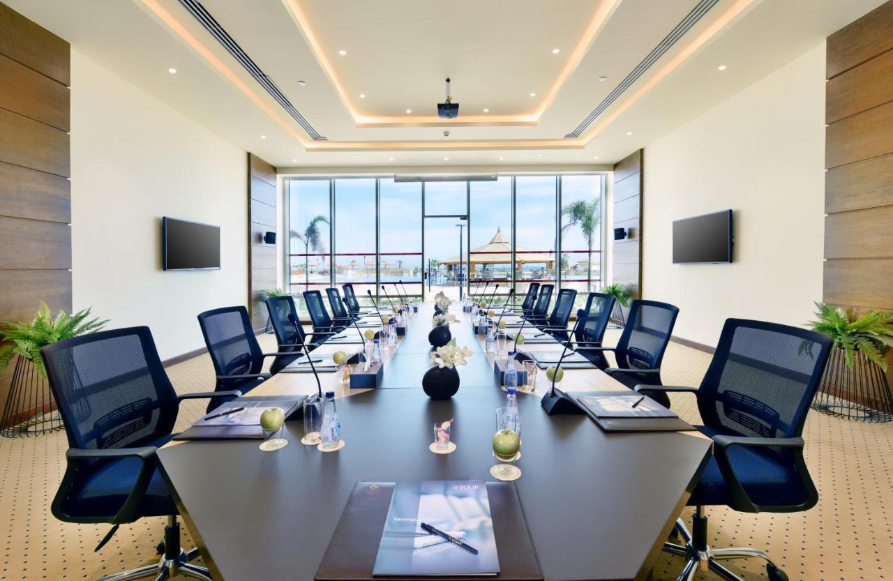 Tolip Resort El Galala Majestic Айн Сохна Екстериор снимка The image shows a modern conference room with a large, dark rectangular table surrounded by ergonomic black chairs. The room features large windows that allow natural light to enter and provide a view of the outdoors, including some greenery. On the 