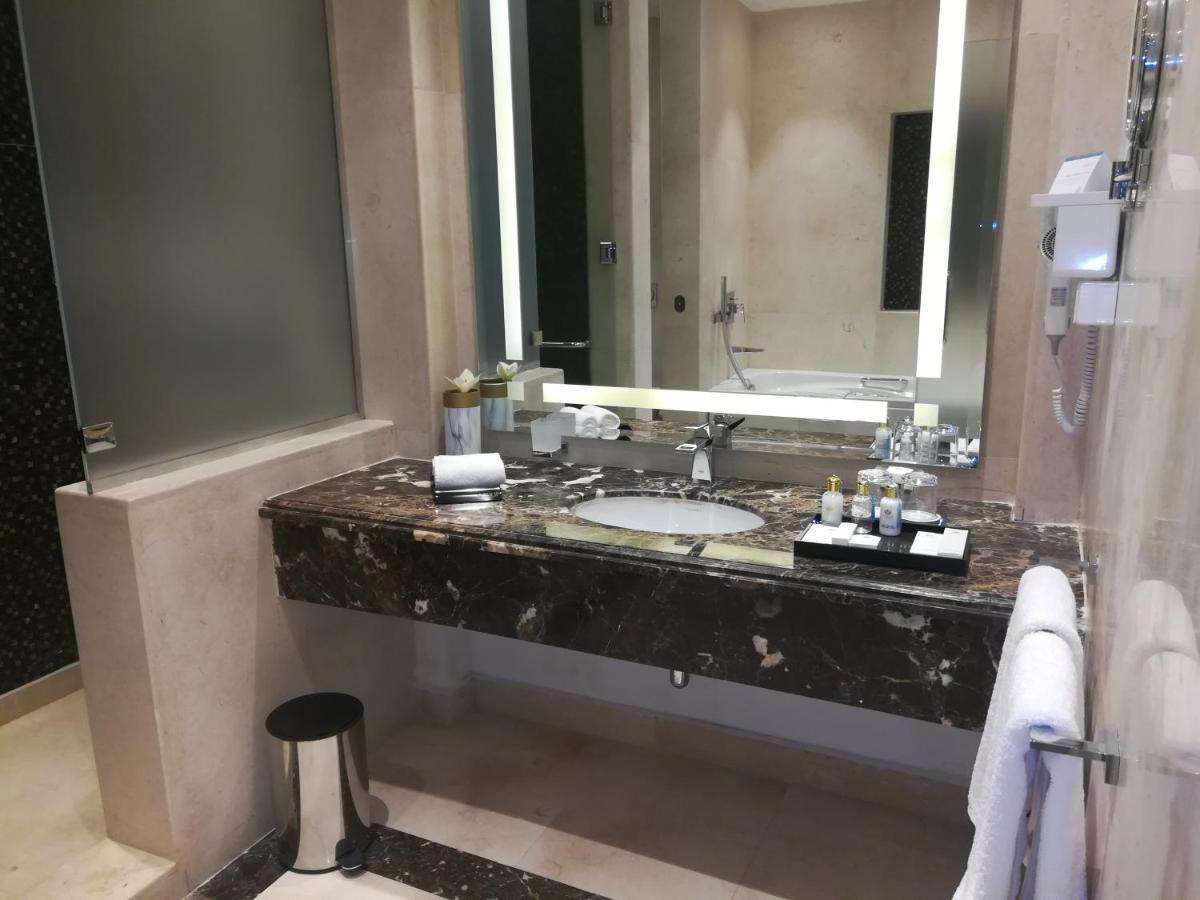 Tolip Resort El Galala Majestic Айн Сохна Екстериор снимка The photo shows a modern bathroom with elegant design features. There is a large vanity made of dark marble with a sink and a set of toiletries neatly arranged on top. A mirror with built-in lighting is mounted above the sink. To the side, there is a