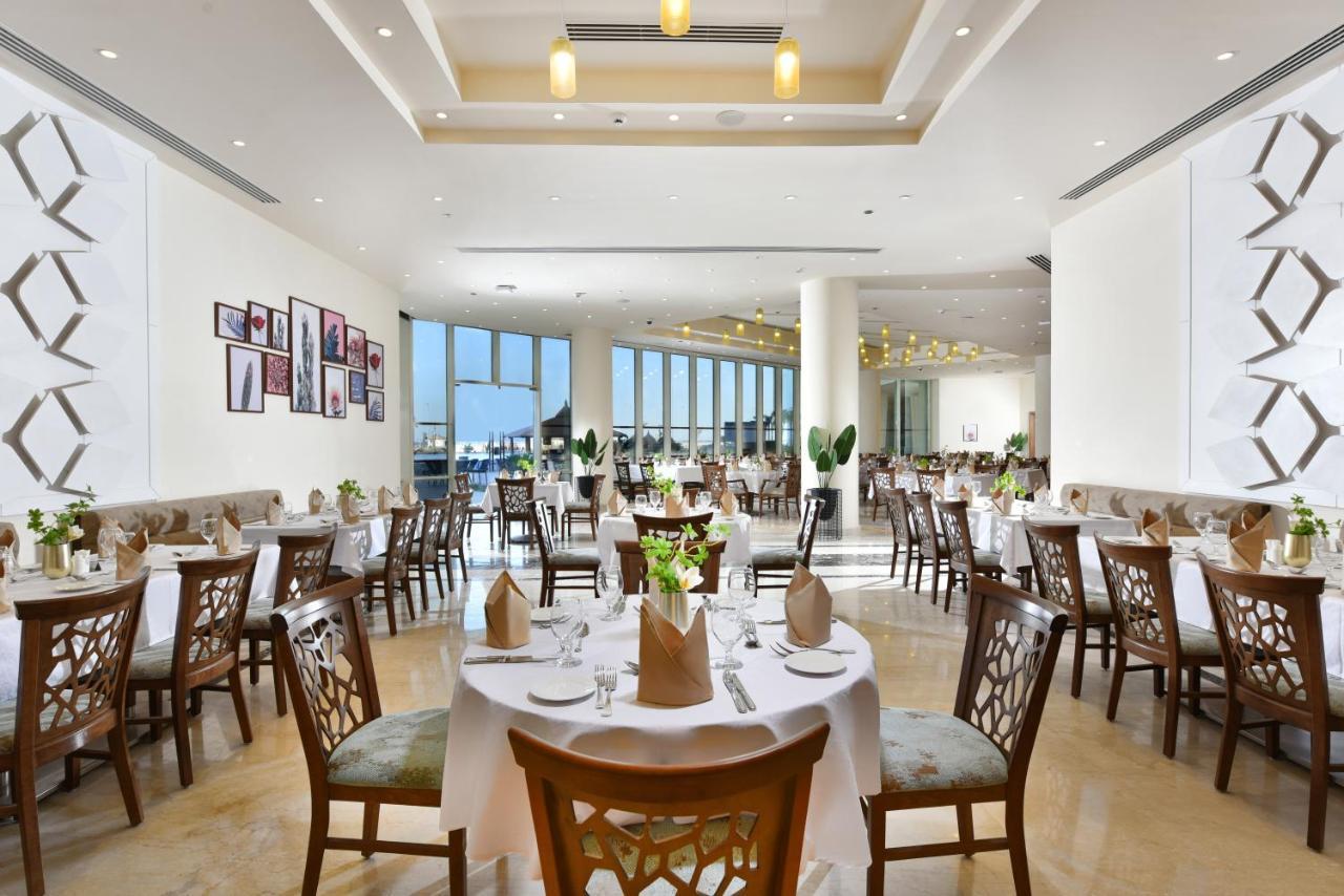 Tolip Resort El Galala Majestic Айн Сохна Екстериор снимка The photo displays a spacious and elegantly designed restaurant interior. It features numerous tables set for dining, with white tablecloths, neatly folded napkins, and decorative centerpieces of flowers. The seating consists of wooden chairs that co