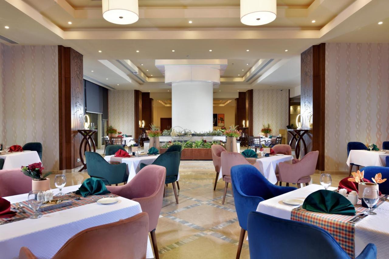 Tolip Resort El Galala Majestic Айн Сохна Екстериор снимка The photo shows a spacious and elegantly designed restaurant interior. The layout includes several round tables dressed in white tablecloths, each set with decorative plates, cutlery, and colorful napkins. The chairs are upholstered in a variety of c