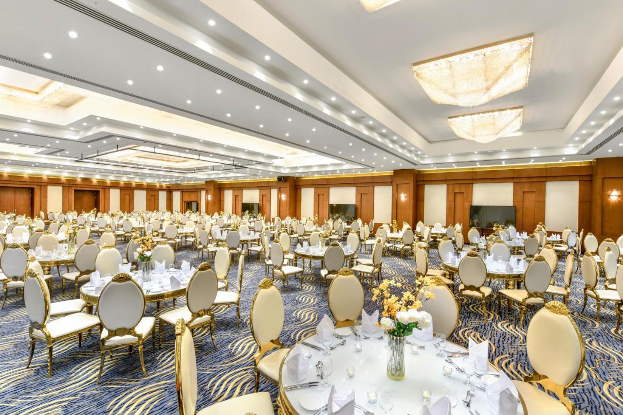 Tolip Resort El Galala Majestic Айн Сохна Екстериор снимка The photo shows a spacious and elegantly decorated banquet hall. The room features numerous round dining tables, each set with white tablecloths and adorned with decorative centerpieces, likely flowers. The chairs surrounding the tables have a luxuri